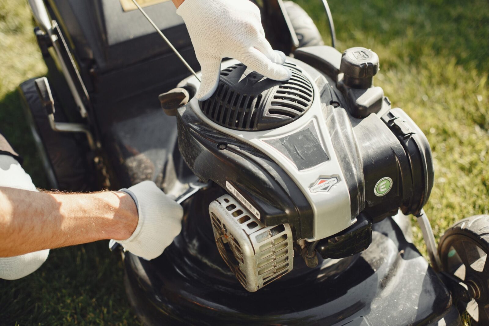 Hands in gloves adjusting a lawn mower outdoors, perfect for gardening themes.